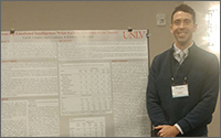 A man in a blue sweater smiling and standing next to a research poster.